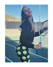 Load image into Gallery viewer, Woman wearing the Hit Happy Tennis Capri Leggings on the tennis court