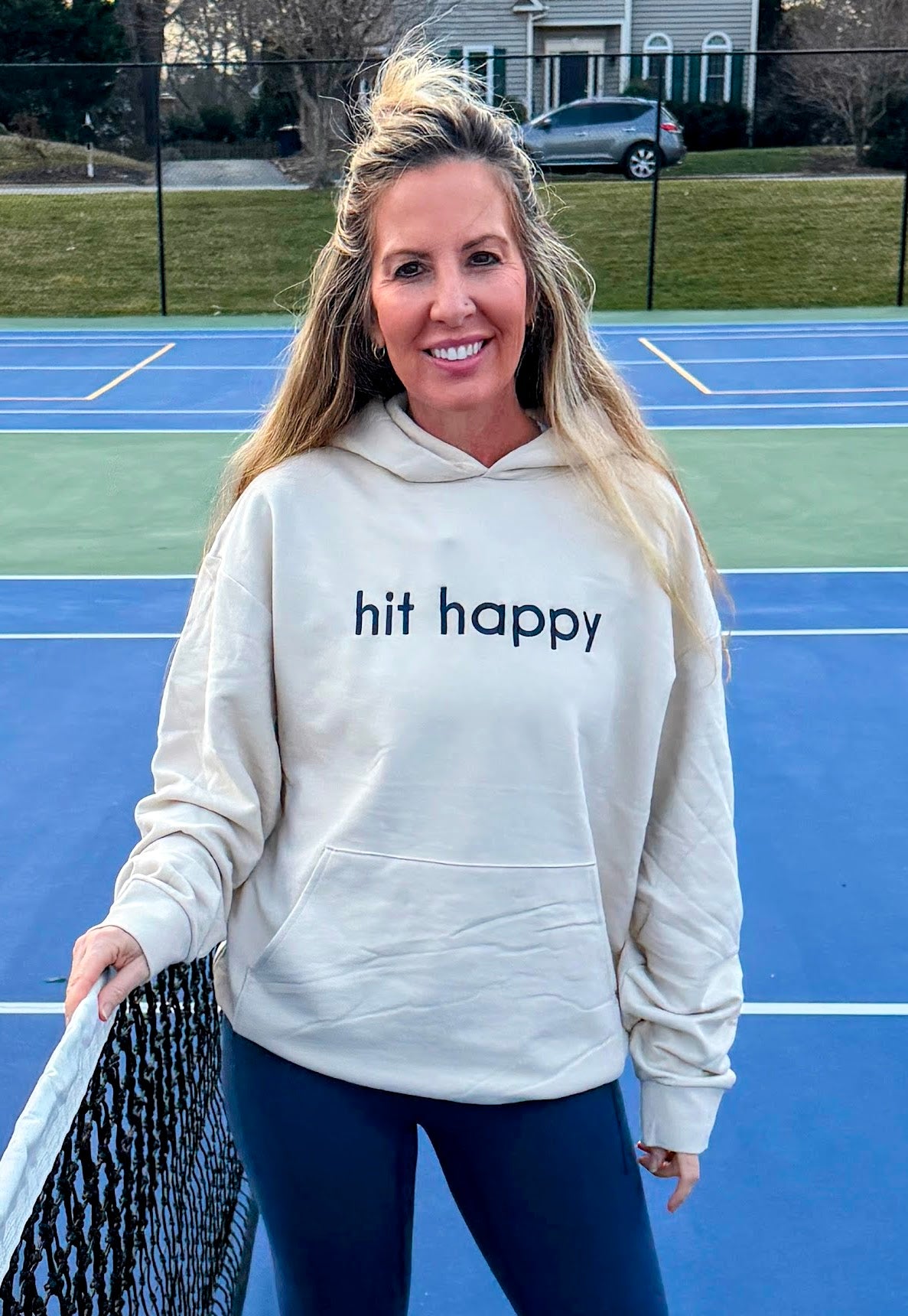 Woman wearing Hit Happy The Icon hoodie on tennis court